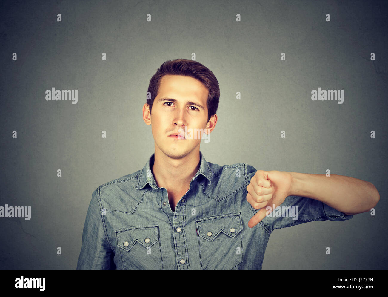 Closeup Portrait zorniger junger Mann mit Daumen runter-Zeichen, in Missbilligung isoliert auf grauem Hintergrund. Negative menschliche Emotion Gesichtsausdruck feelin Stockfoto
