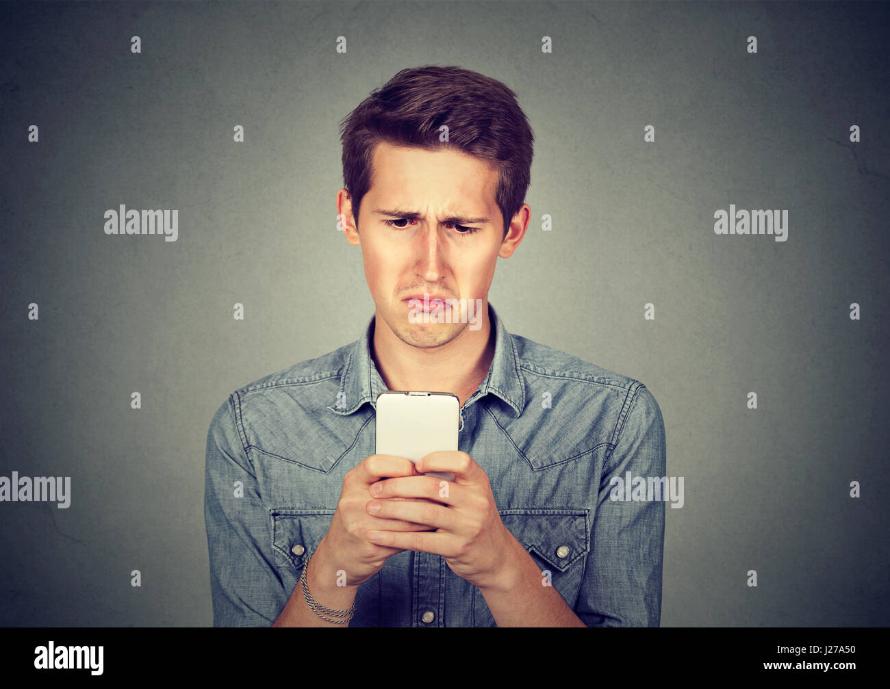 Verärgert gestressten Mann hält Handy angewidert mit Nachricht erhielt er isoliert auf grauem Hintergrund. Menschliches Gesicht Ausdruck Emotion Gefühl Wahrnehmung Stockfoto