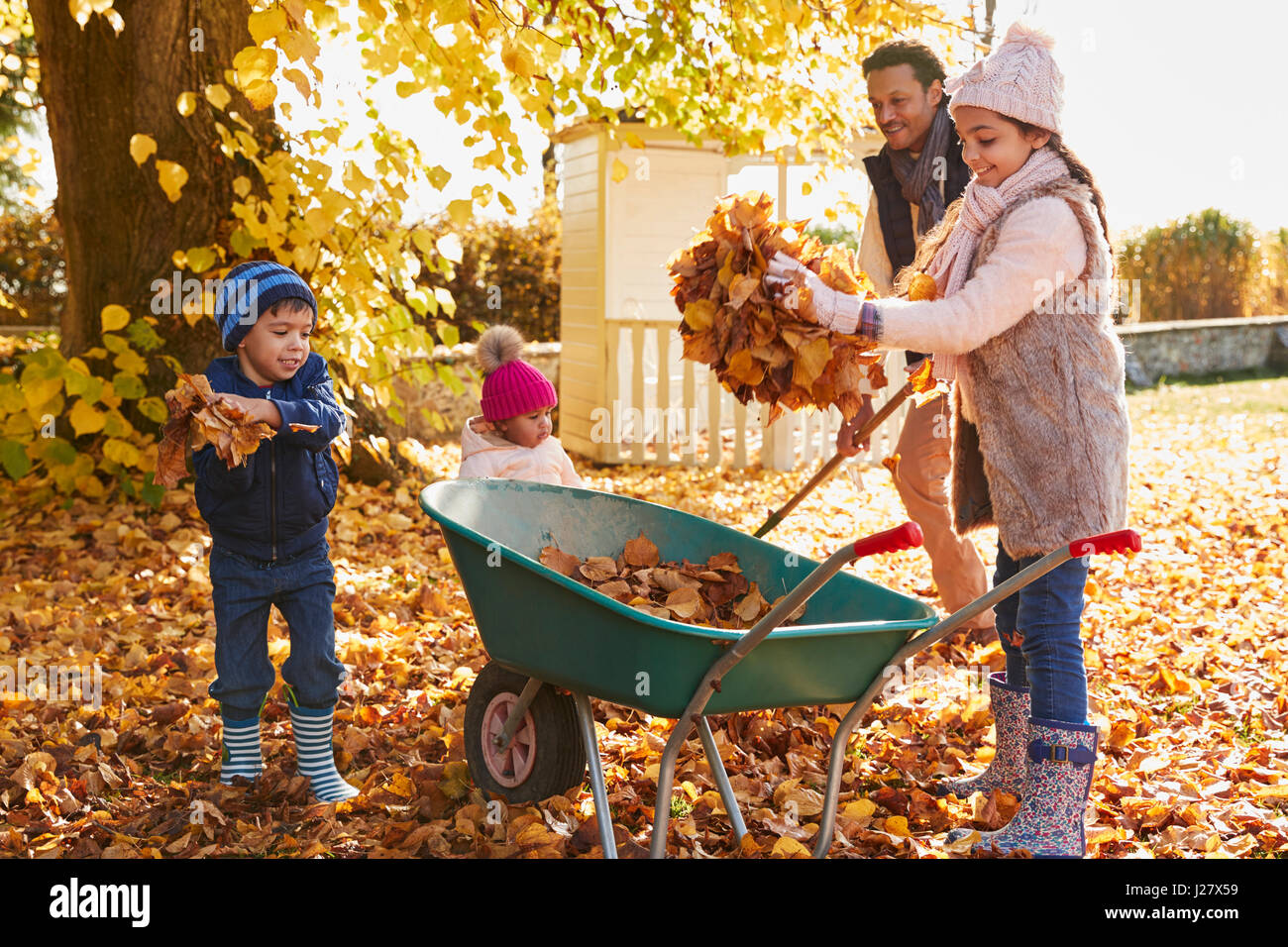 Vater der Kinder helfen, Herbstlaub im Garten sammeln Stockfoto