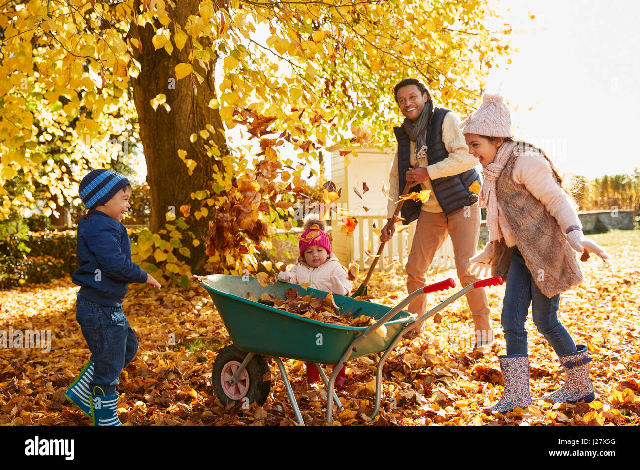 Vater der Kinder helfen, Herbstlaub im Garten sammeln Stockfoto