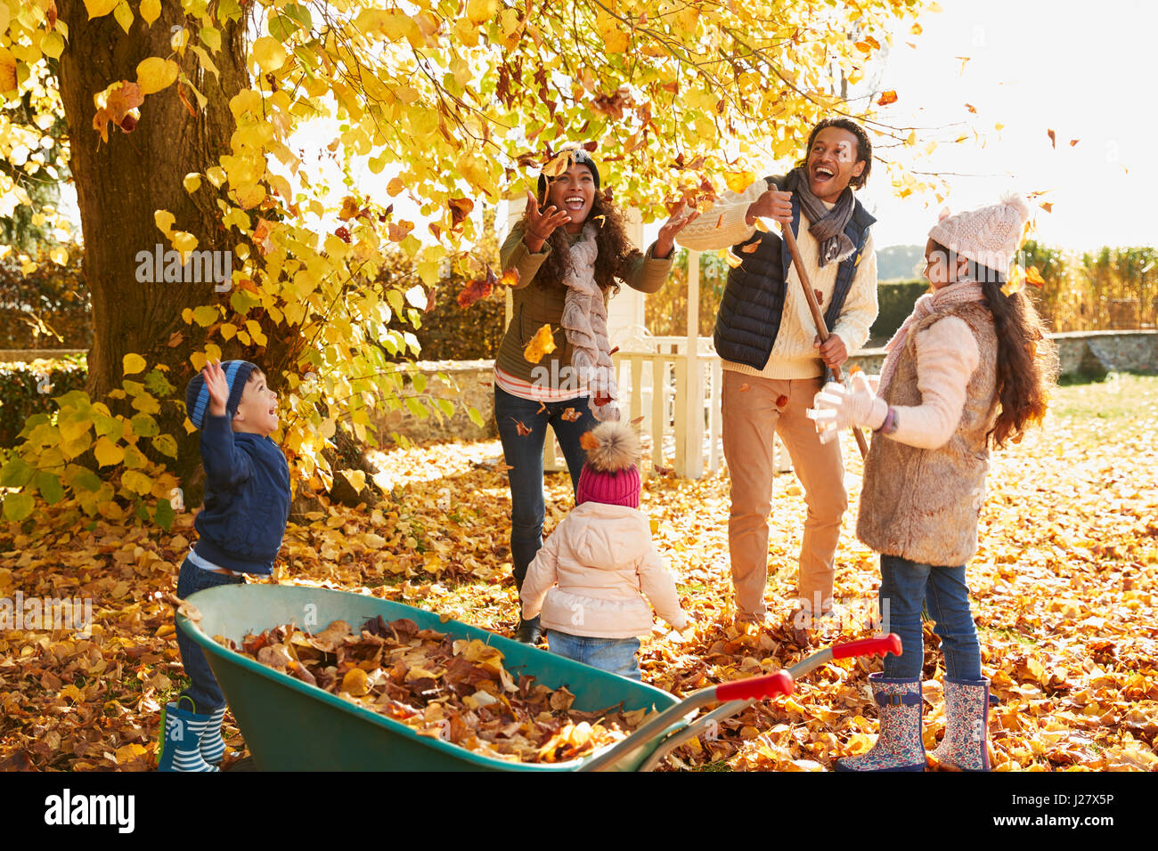 Kinder helfen Eltern, Herbstlaub im Garten sammeln Stockfoto