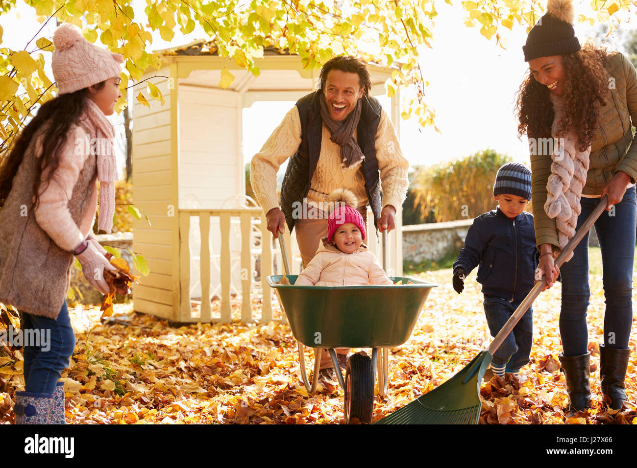 Kinder helfen Eltern, Herbstlaub im Garten sammeln Stockfoto