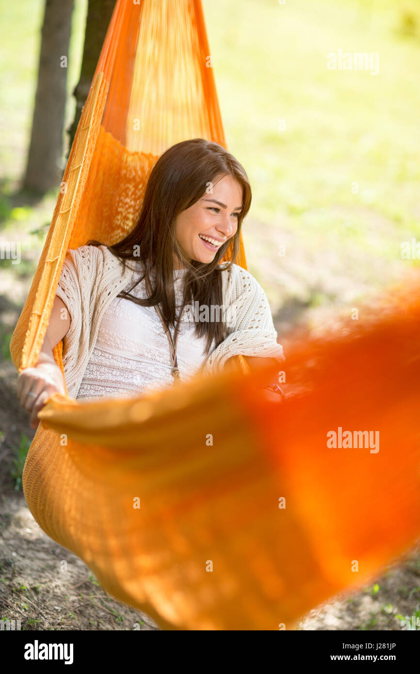 Sympathische junge Frau liegend und in orange Hängematte im Freien genießen Stockfoto