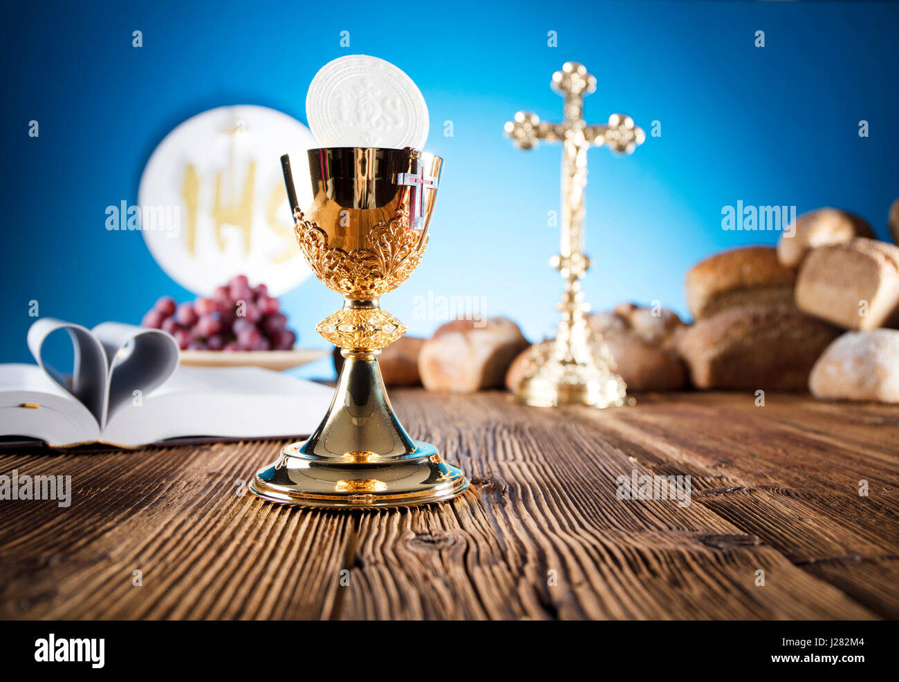 Erste Heilige Kommunion. Katholische Religion-Thema. Kruzifix, Bibel, Brot auf rustikalen Holztisch und blauem Hintergrund. Stockfoto