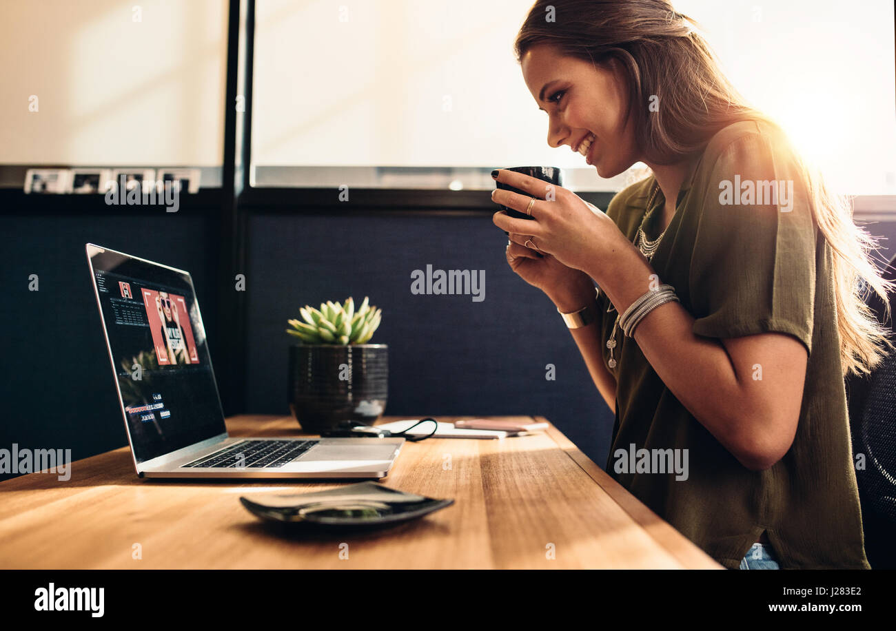 Junge Frau, die Bearbeitung von Videos auf ihrem Laptop beim Kaffeetrinken. Vloggerin ihr Vlog mit einer Tasse Kaffee zu genießen. Stockfoto