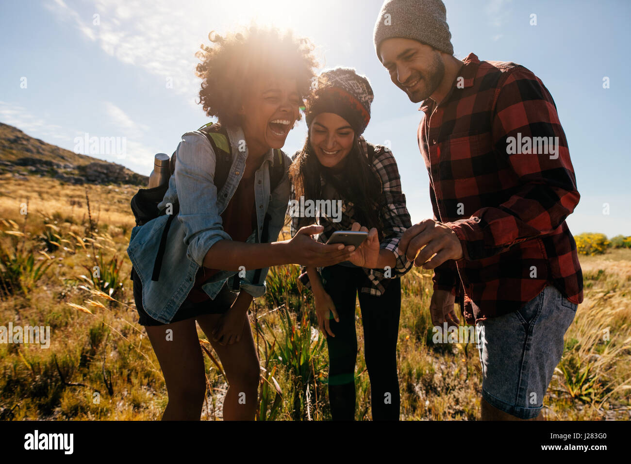 Gruppe von Wanderern betrachten von Bildern auf dem Handy und lachen. Glückliche junge Menschen wandern im Land. Stockfoto
