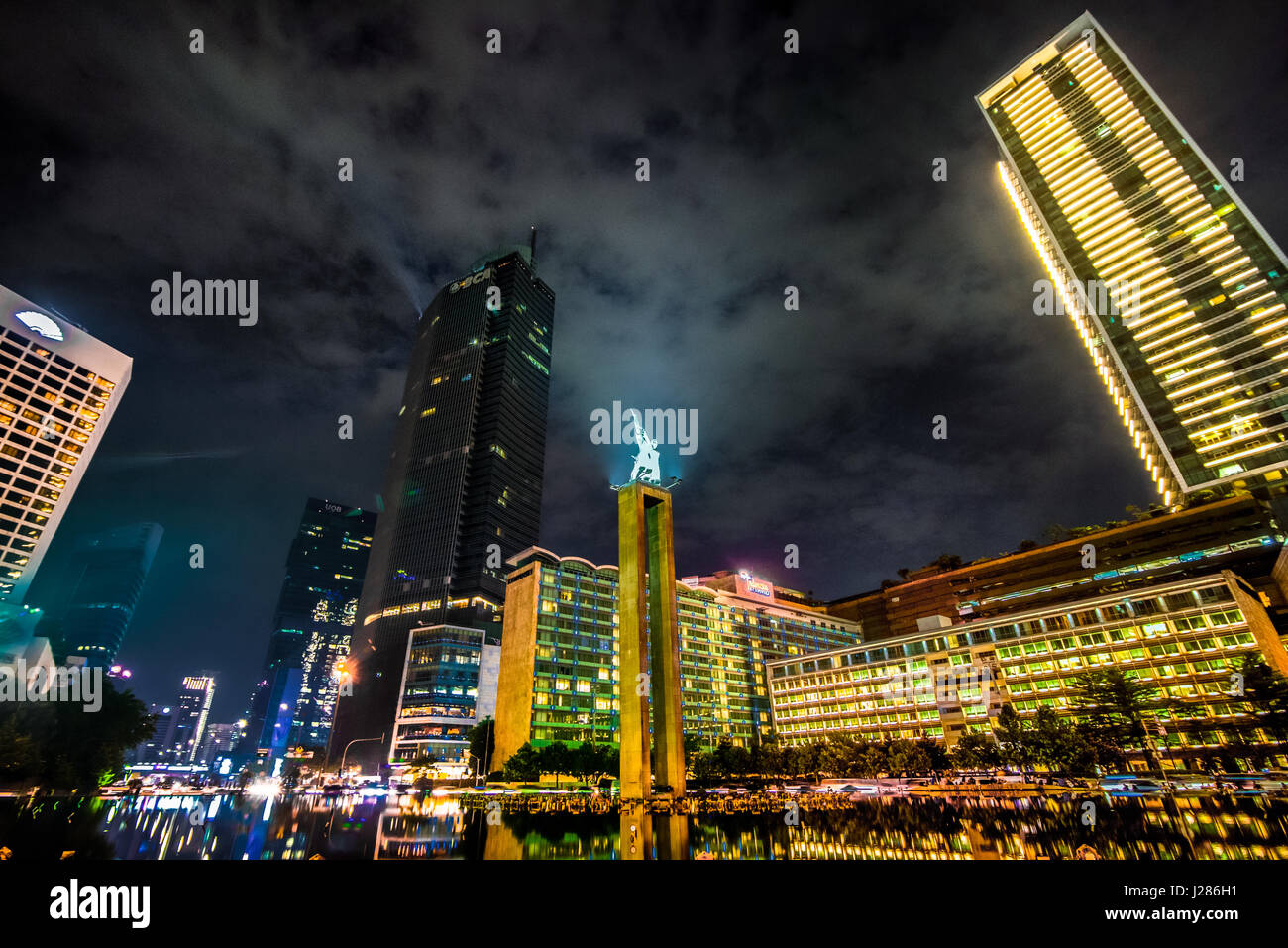 Willkommen-Denkmal im Herzen von Jakarta in der Nacht, umgeben von hohen Gebäuden in der Region bekannt als Bundaran HI. Stockfoto