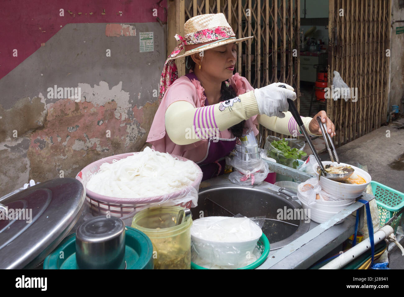 Frau Streetfood Anbieter schöpfen von Suppe und Nudeln für einen Kunden in Bangkok, Thailand Stockfoto