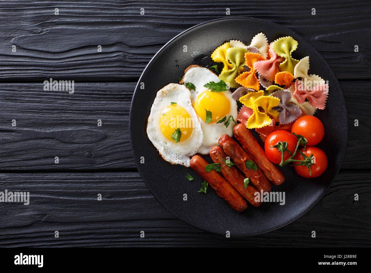 herzhaftes Frühstück: gebratenen Eiern, Würstchen, Farfalle Pasta und Tomaten Nahaufnahme auf einer Platte. Horizontale Ansicht von oben Stockfoto