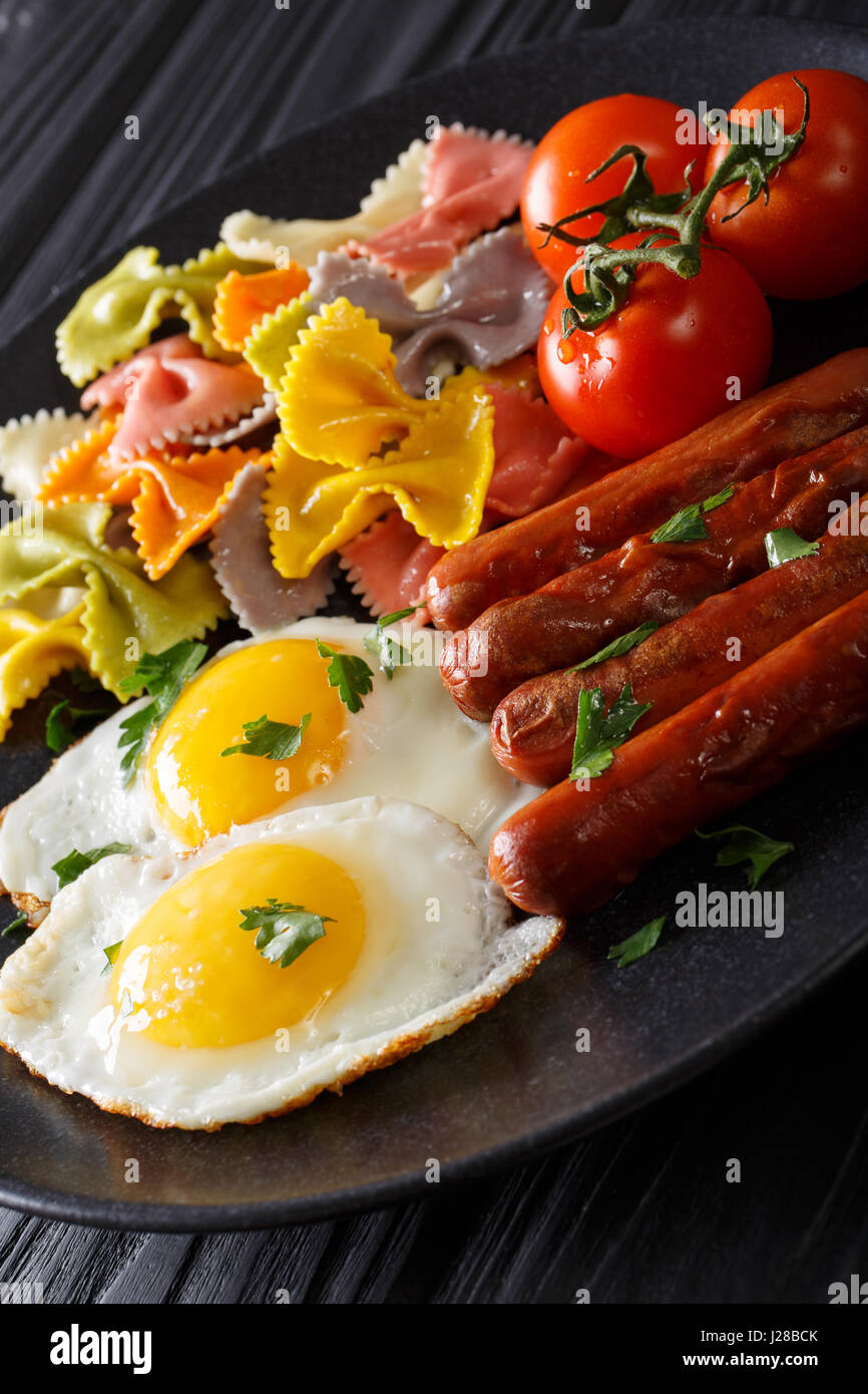 herzhaftes Frühstück: gebratenen Eiern, Würstchen, Farfalle Pasta und Tomaten Nahaufnahme auf einer Platte. vertikale Stockfoto