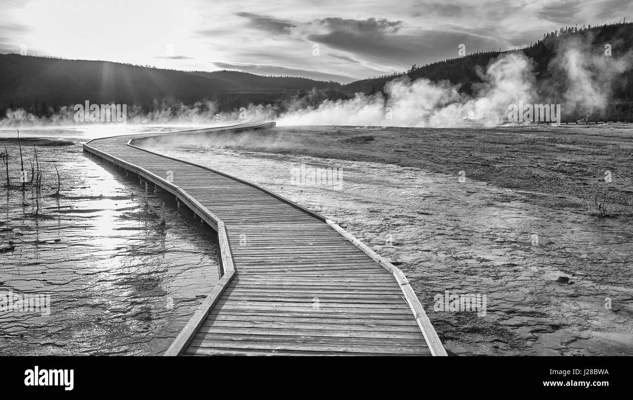 Schwarz / weiß Bild einer hölzernen Brücke über dampfenden Terrain im Yellowstone National Park bei Sonnenuntergang, Wyoming, USA. Stockfoto