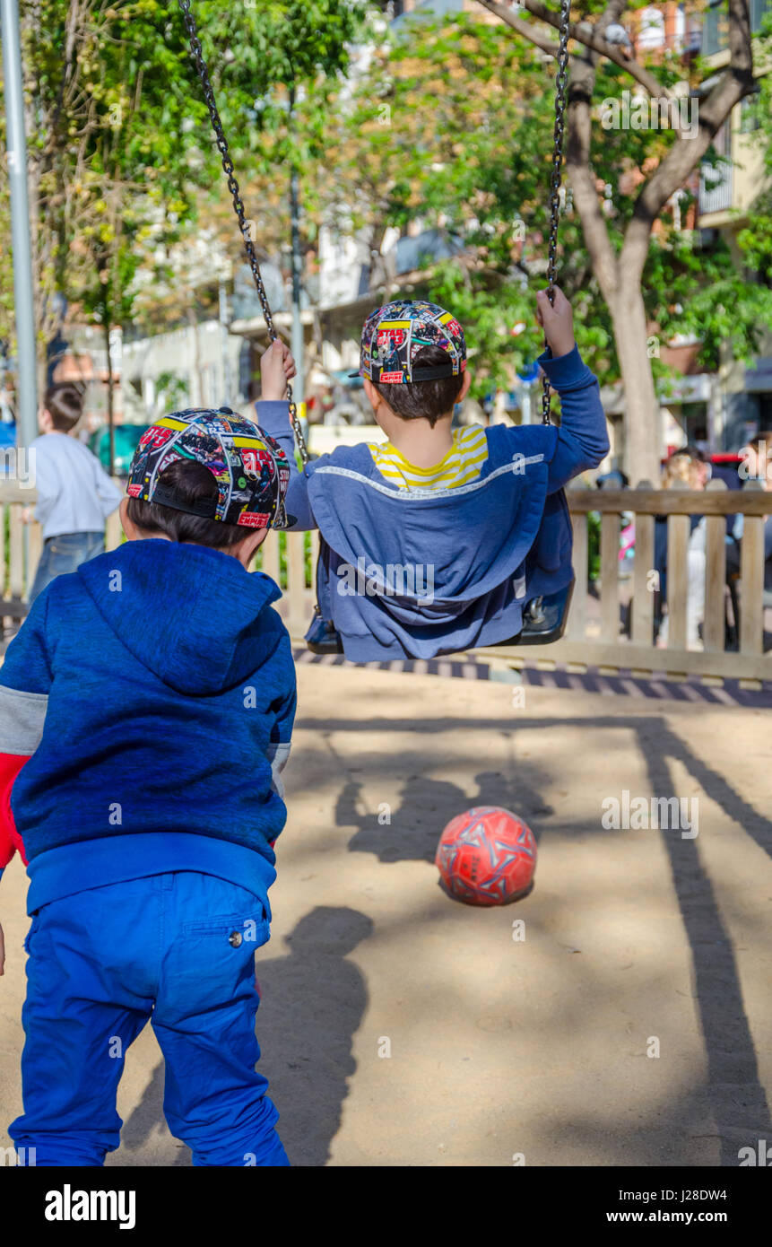 Ein kleiner Junge schiebt seinen älteren Bruder, der auf einer Schaukel auf einem Spielplatz spielen. Stockfoto