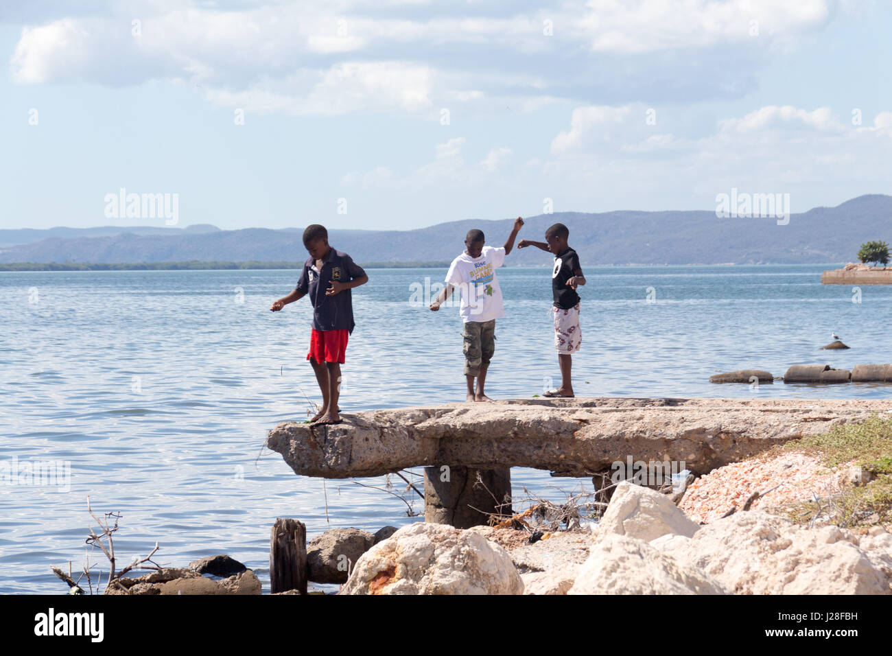 Jamaika, Kingston, Balancing act, drei Kinder balancieren auf die Felsformation oberhalb des Wassers Stockfoto
