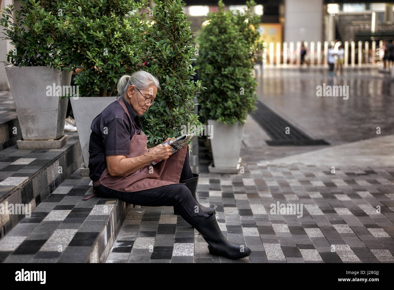 Frau eine Pause von der Arbeit und die Zeitung draußen auf der Straße saß.  Bangkok, Thailand, Stockfoto