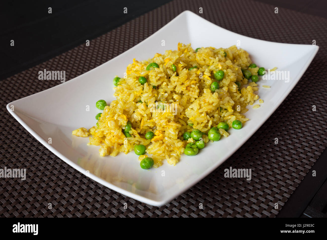 Gebratener curry-Reis mit Erbsen serviert auf weißen Teller im Restaurant, braunen Hintergrund. Stockfoto