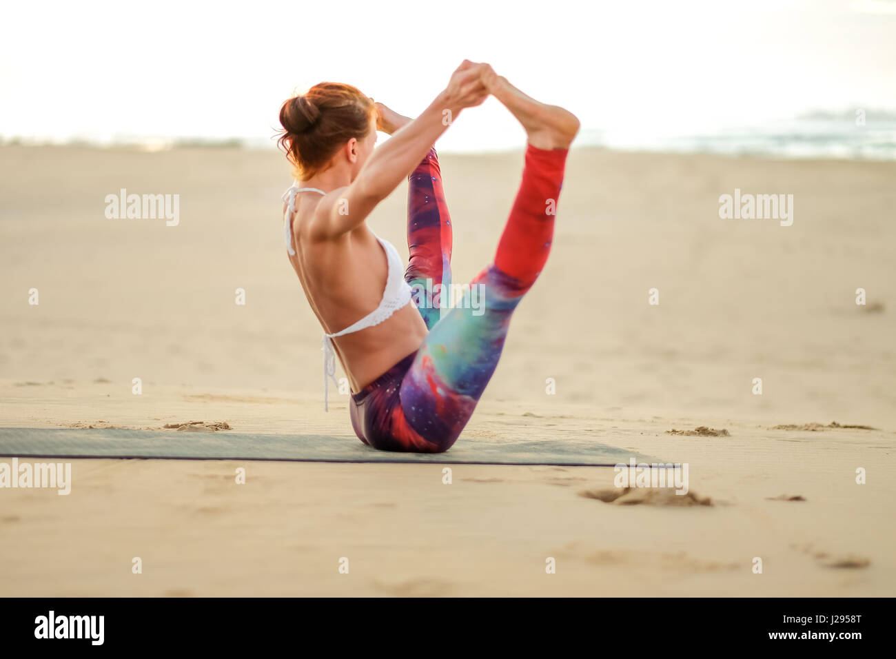 Ein Yogi oder Yoga Meister Lehrer übt bei Sonnenaufgang am Strand und zeigt ihre Stärke, Kontrolle und Technik in den frühen Morgenstunden. Stockfoto