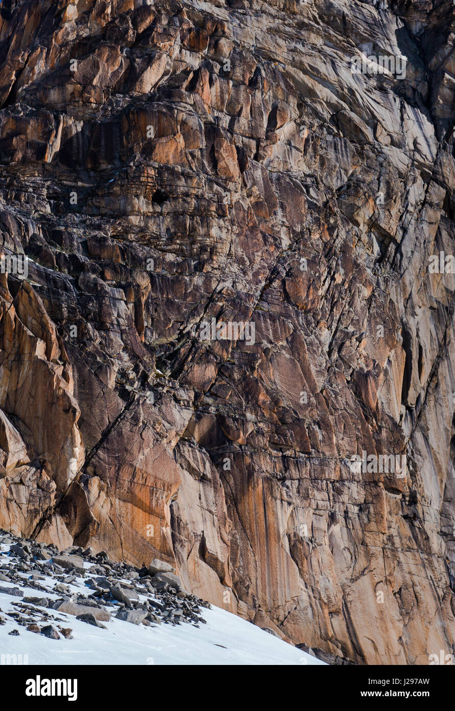 Erodierten Felsen Granitwand mit mehreren Rissen in verschiedenen Schattierungen von Eisen rot und grau und Flecken von Schnee im winter Stockfoto