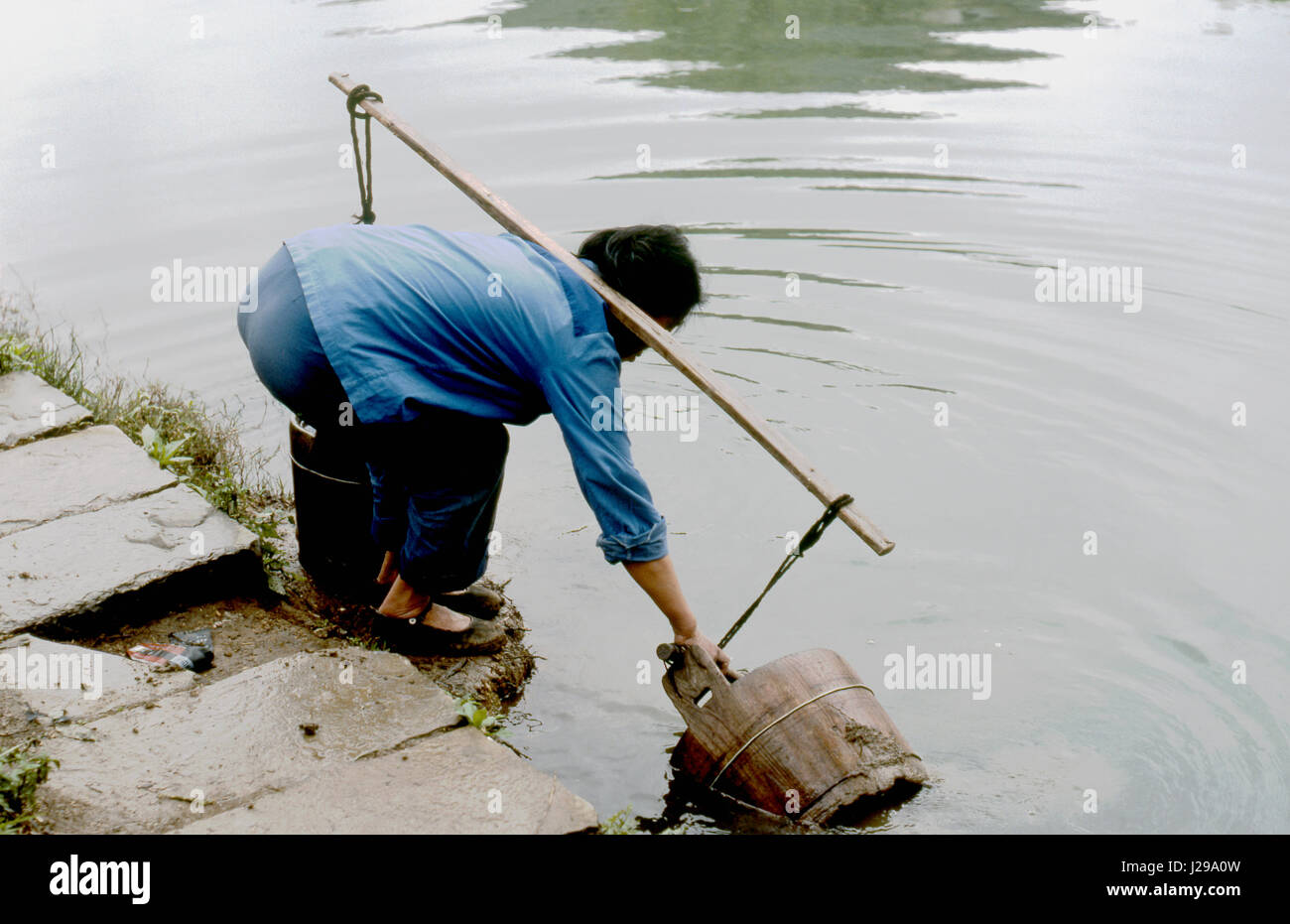 Frau mit Eimer Wasser vom Fluss zu holen, Provinz Guizhou, China. Stockfoto