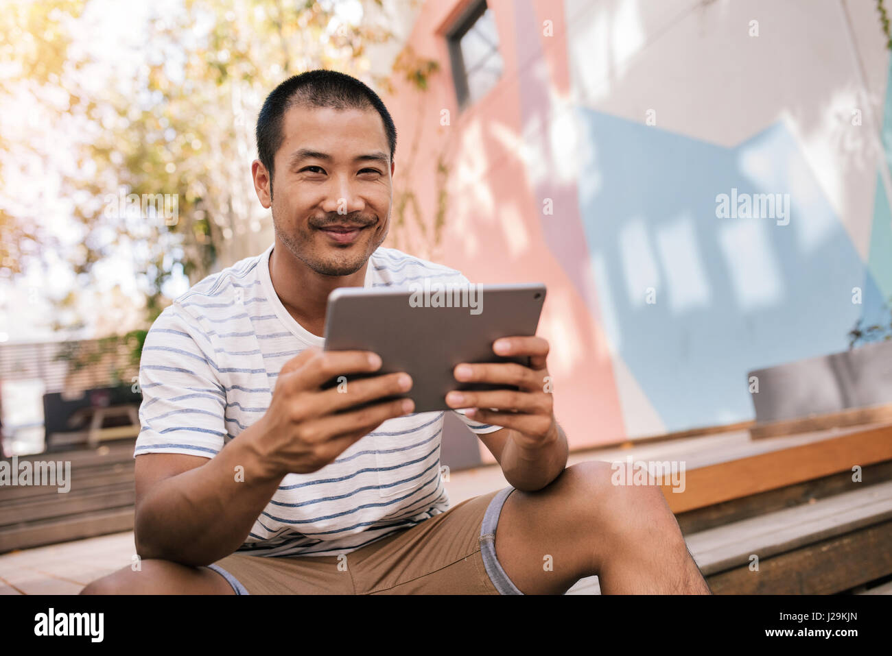 Lächelnd asiatischen Mann sitzt auf der Treppe draußen mit einem tablet Stockfoto