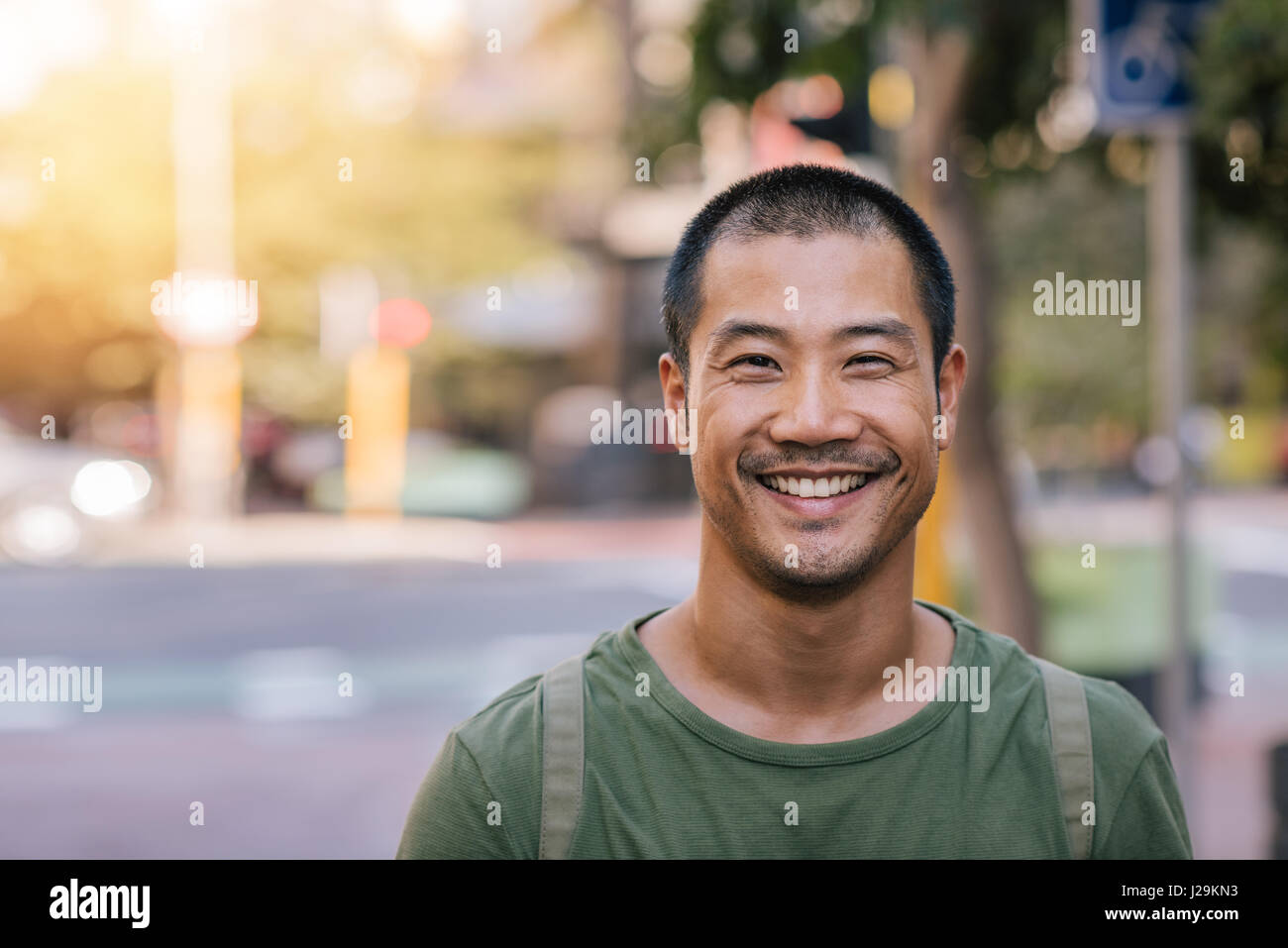 Junge asiatische Mann lächelnd souverän auf einer Stadtstraße Stockfoto