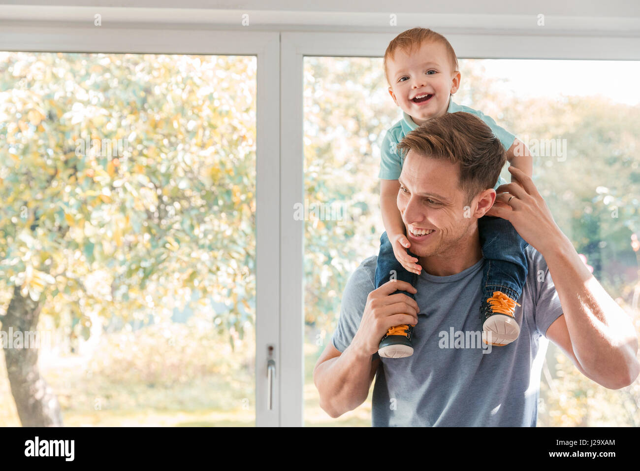 Kleinkind Jungen auf Vaters Schultern zu Hause Fenster Stockfoto