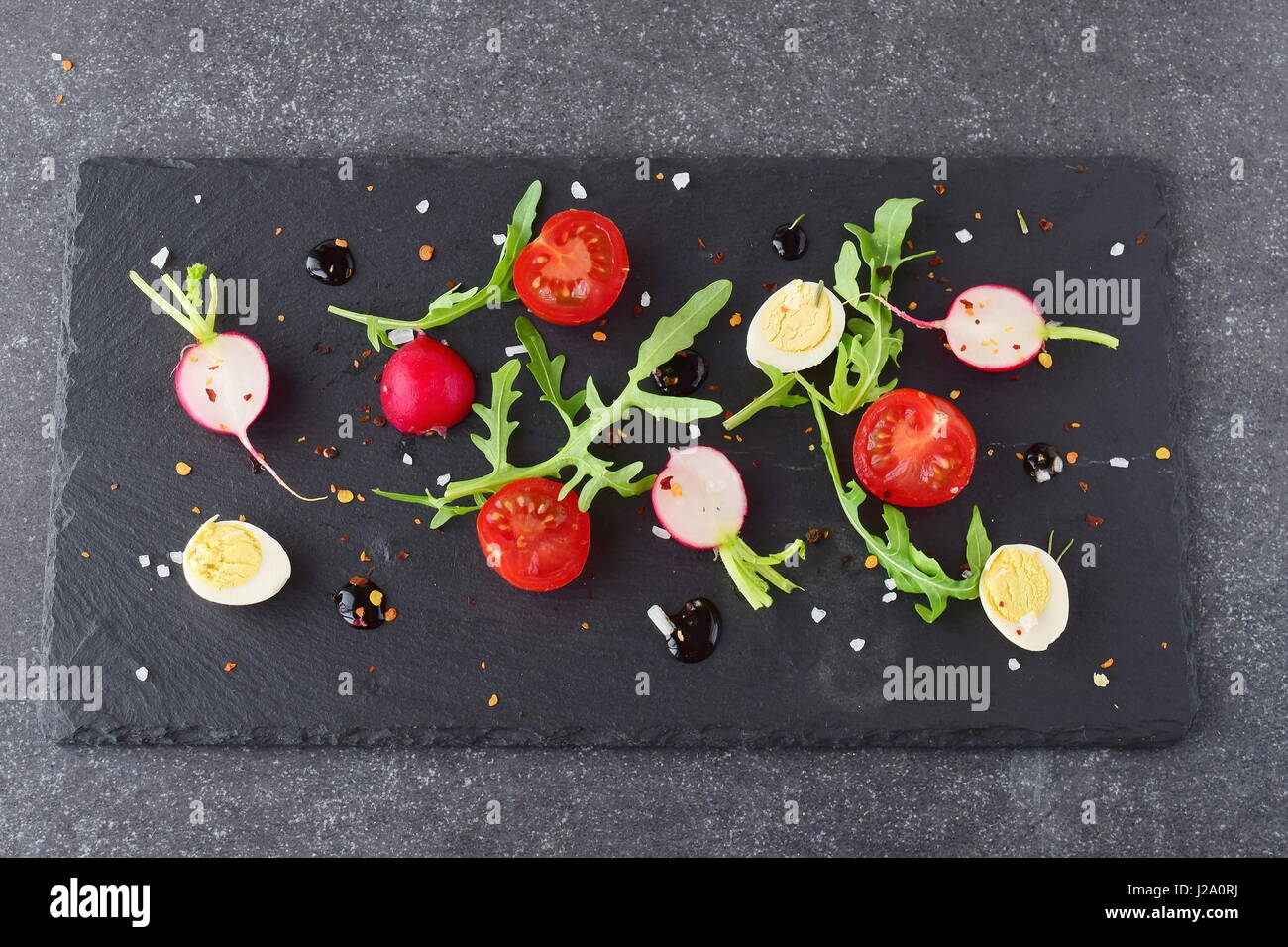 Frische Radieschen, Kirschtomaten, Wachtelei, Parmeggiano mit Balsamico-Glasur auf einem schwarzen Steinplatte. Mediterranes Lebensgefühl. Gesunde Ernährung. Stockfoto