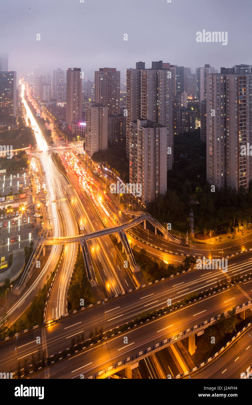 China, Chongqing, erhöhte Ansicht des Verkehrs auf massiven Autobahnen umgeben von Apartment-Türme in der Abenddämmerung an regnerischen Herbstabend Stockfoto