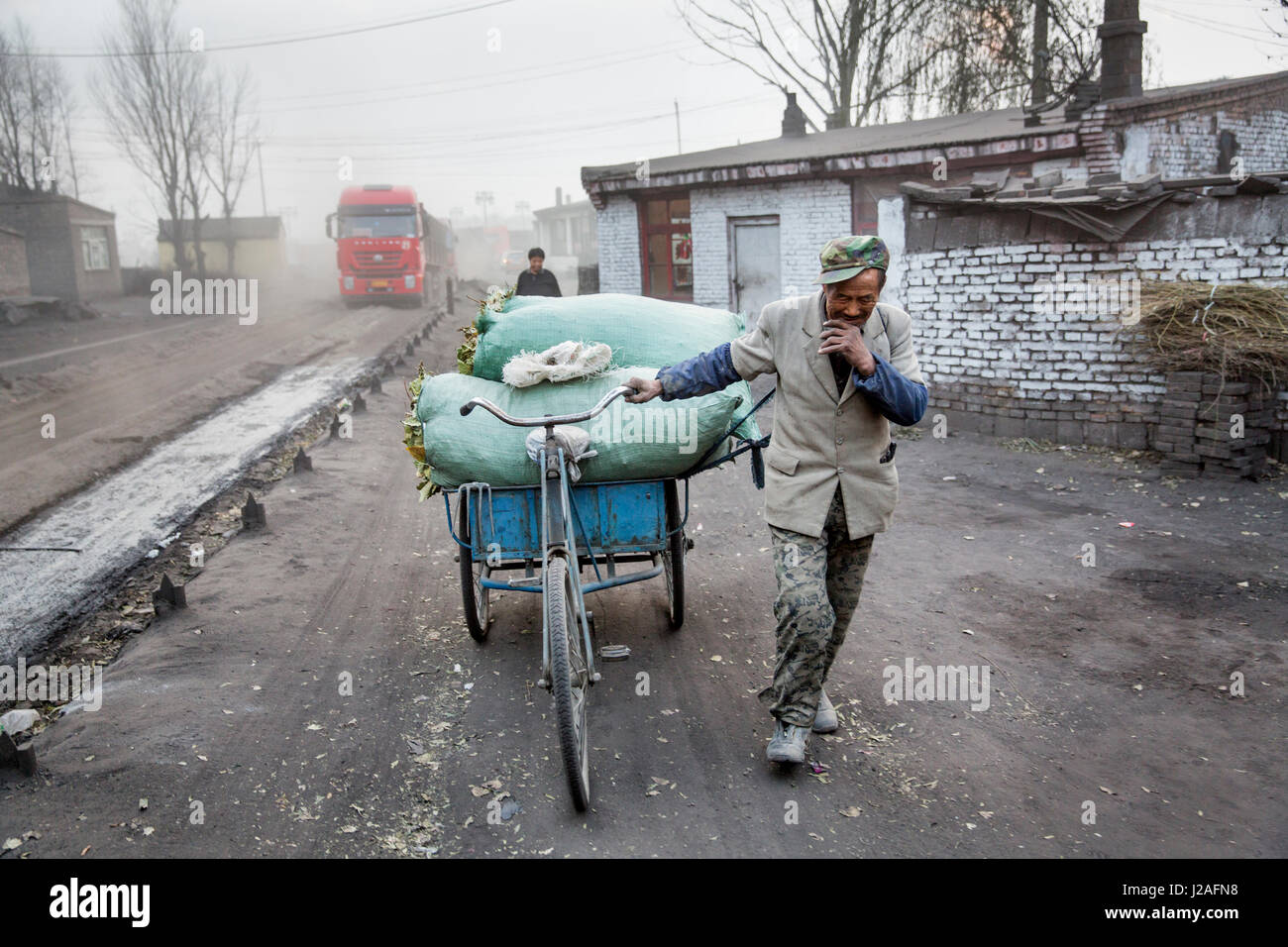 China, Provinz Shanxi, Datong, Porträt von älteren Mann zu Fuß Fracht beladen Dreirad an Staub bedeckten Zufahrtsstraße verwendet, um Kohle zu Datong Nr. 2 Kraftwerk liefern Stockfoto