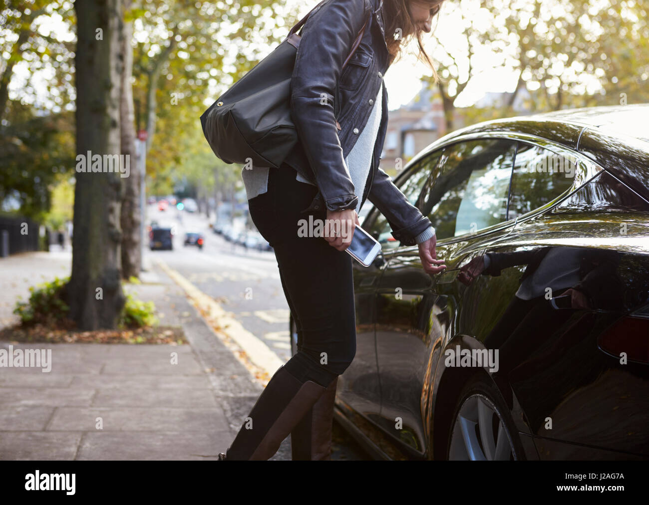 Junge Frau mit Handy immer in der Rückseite eines Autos Stockfoto