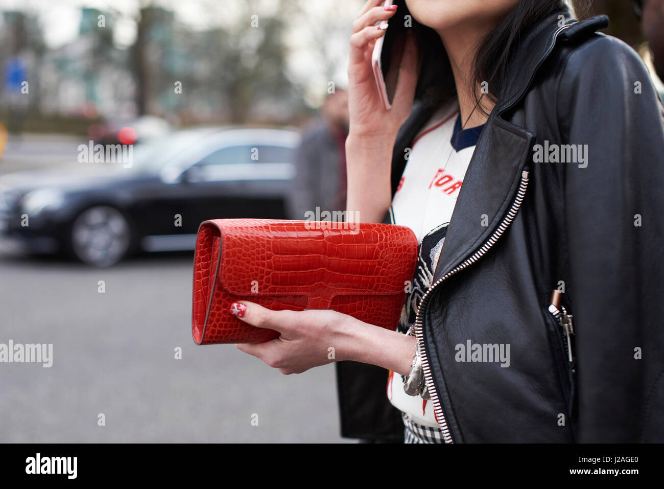 LONDON - Februar 2017: Mittelteil Nahaufnahme von Frau trägt eine schwarze Lederjacke Fahrrad, eine rote Hermes Handtasche halten und mittels Smartphone auf der Straße während der London Fashion Week, horizontale Stockfoto