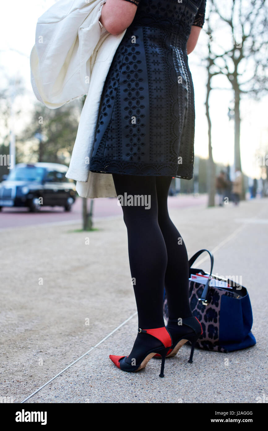 LONDON - Februar 2017: Niedrige Abschnitt Frau mit schwarzen und roten Stiletto Pumps und schwarzen gemusterten Kleid während der London Fashion Week am Straßenrand stehen, vertikal, rückseitige Ansicht Stockfoto