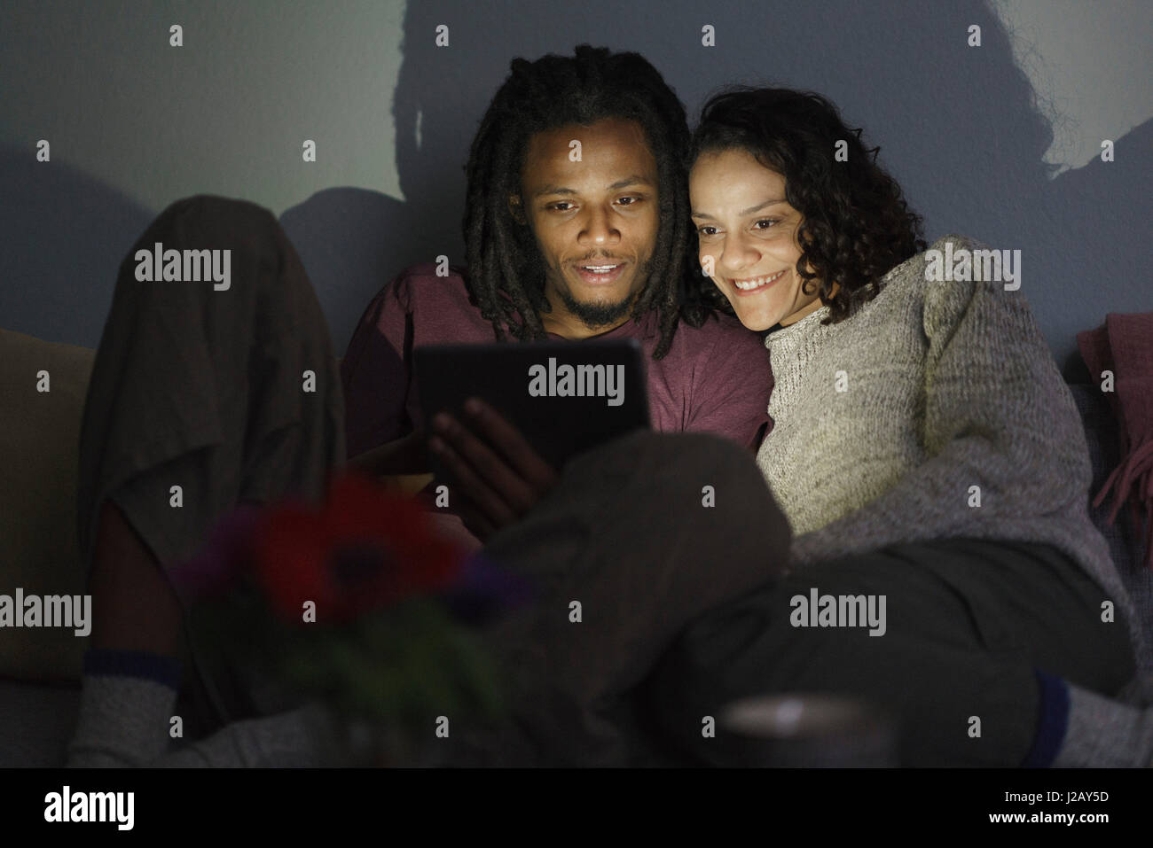 Lächelnde multiethnischen paar mit digital-Tablette im dunklen Wohnzimmer Stockfoto