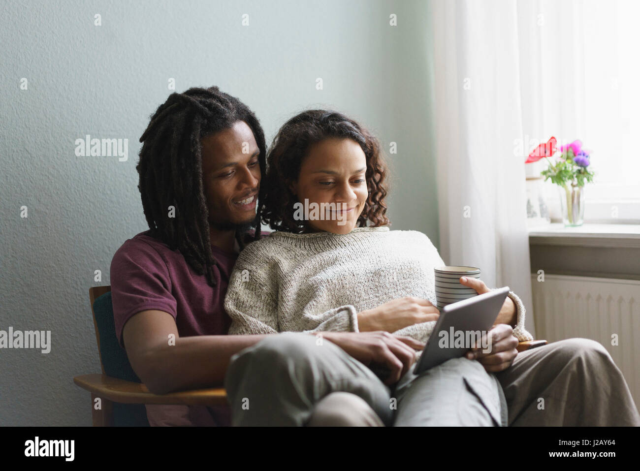 Multi-ethnischen Pärchen mit digital-Tablette während sitzt auf Sessel zu Hause Stockfoto