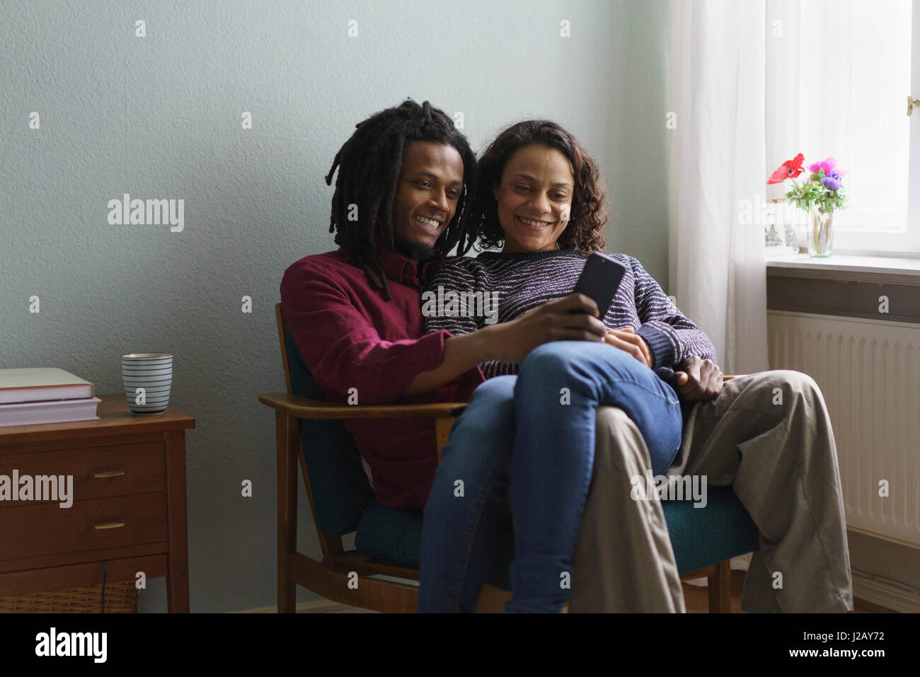 Lächelnd multiethnischen paar mit Smartphone auf Sessel zu Hause sitzend Stockfoto