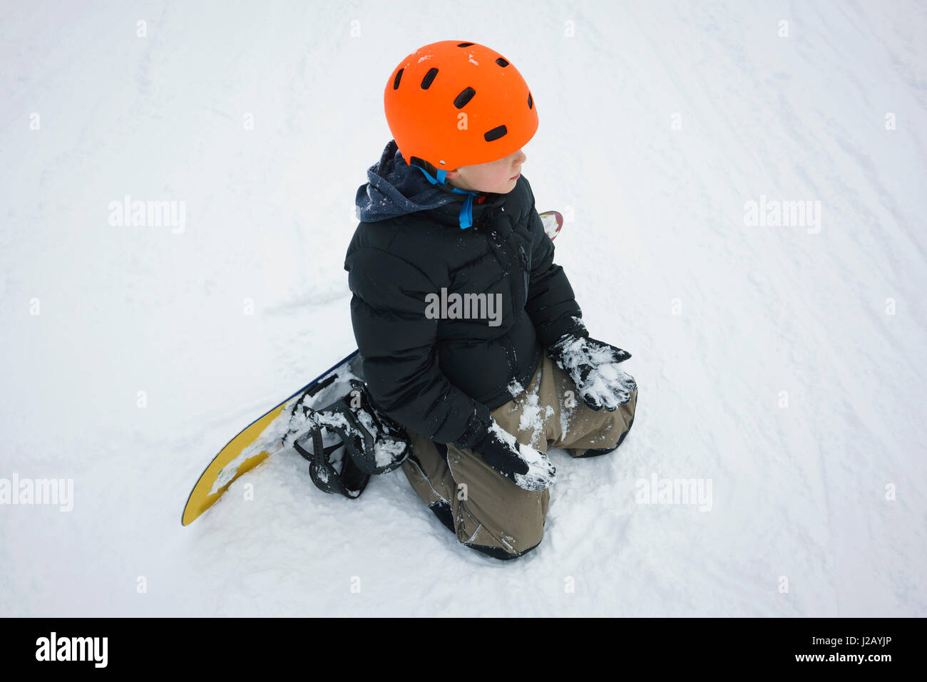 Erhöhte Ansicht eines jungen mit Snowboard kniend im Schnee Stockfoto