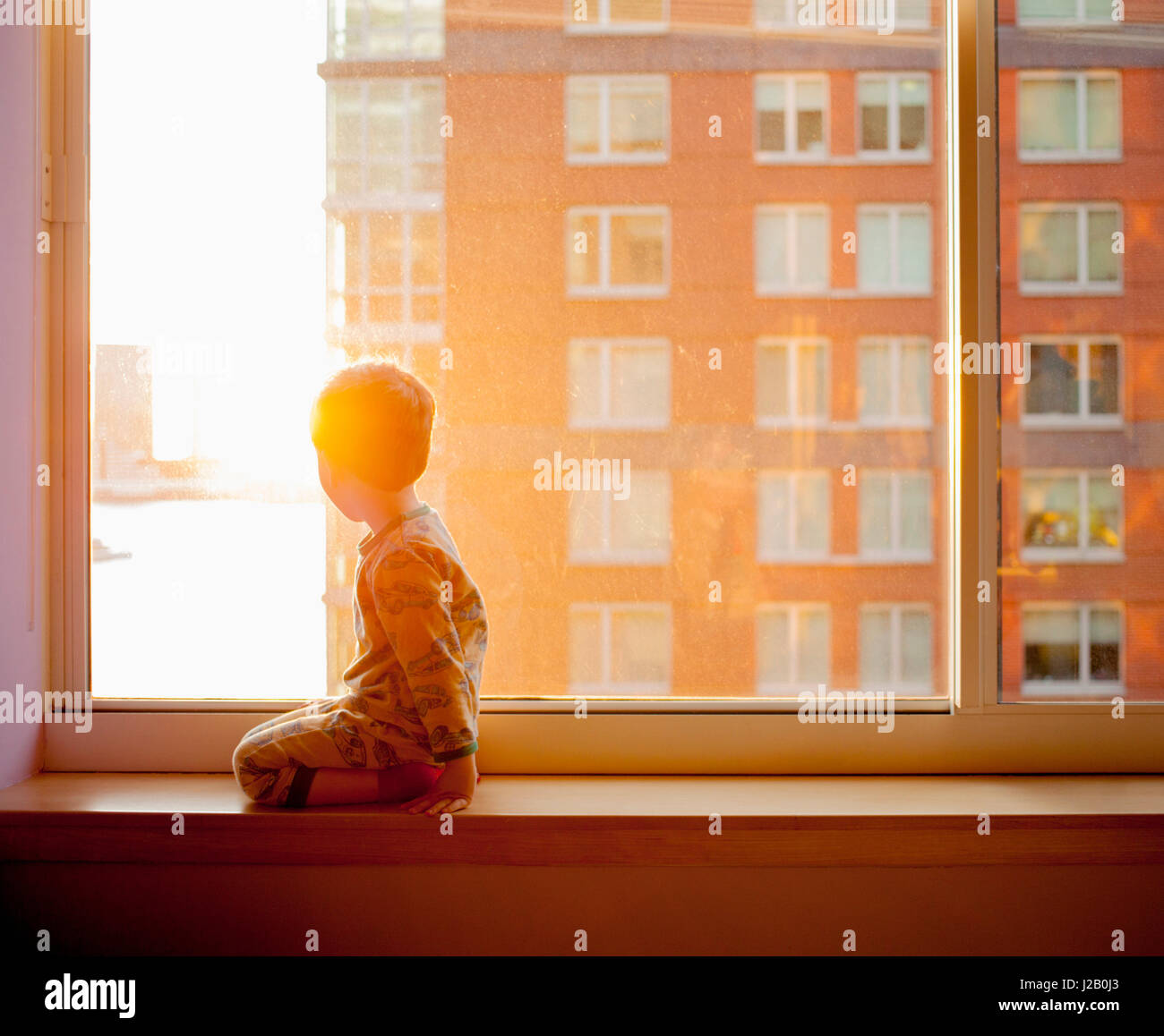 Seitenansicht des jungen suchen kniend auf Fensterbank zu Hause Stockfoto