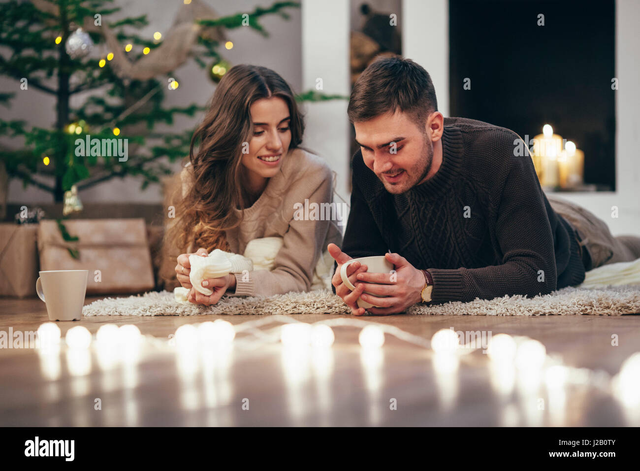 Lächelnde paar Kaffeetrinken liegend auf Teppich zu Hause während der Weihnachtszeit Stockfoto