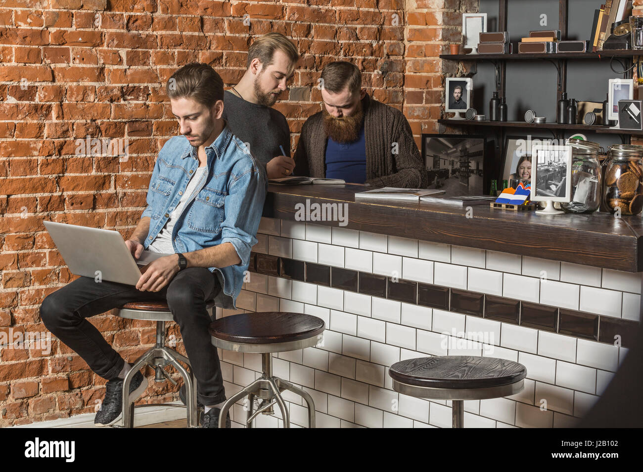Junge mit Laptop, während Kollegen diskutieren gegen Wand bei Friseur Ziegel Friseur Stockfoto