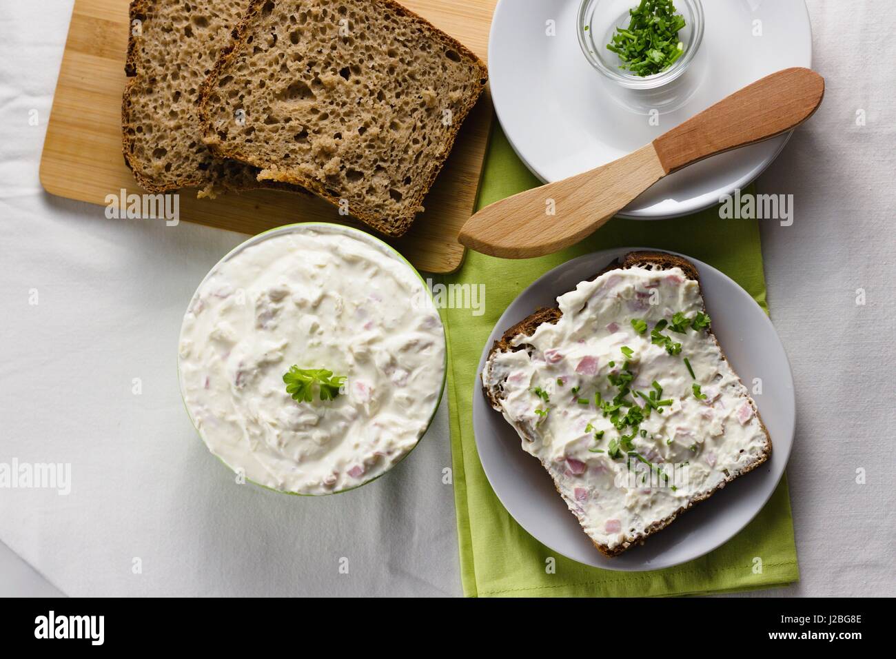 Scheibe Roggen-Vollkornbrot mit zarten hellen und frischen Quark Ausbreitung mit Schnittlauch und Petersilie bestreut. Verbreitung von Messer und einige e Holz Stockfoto