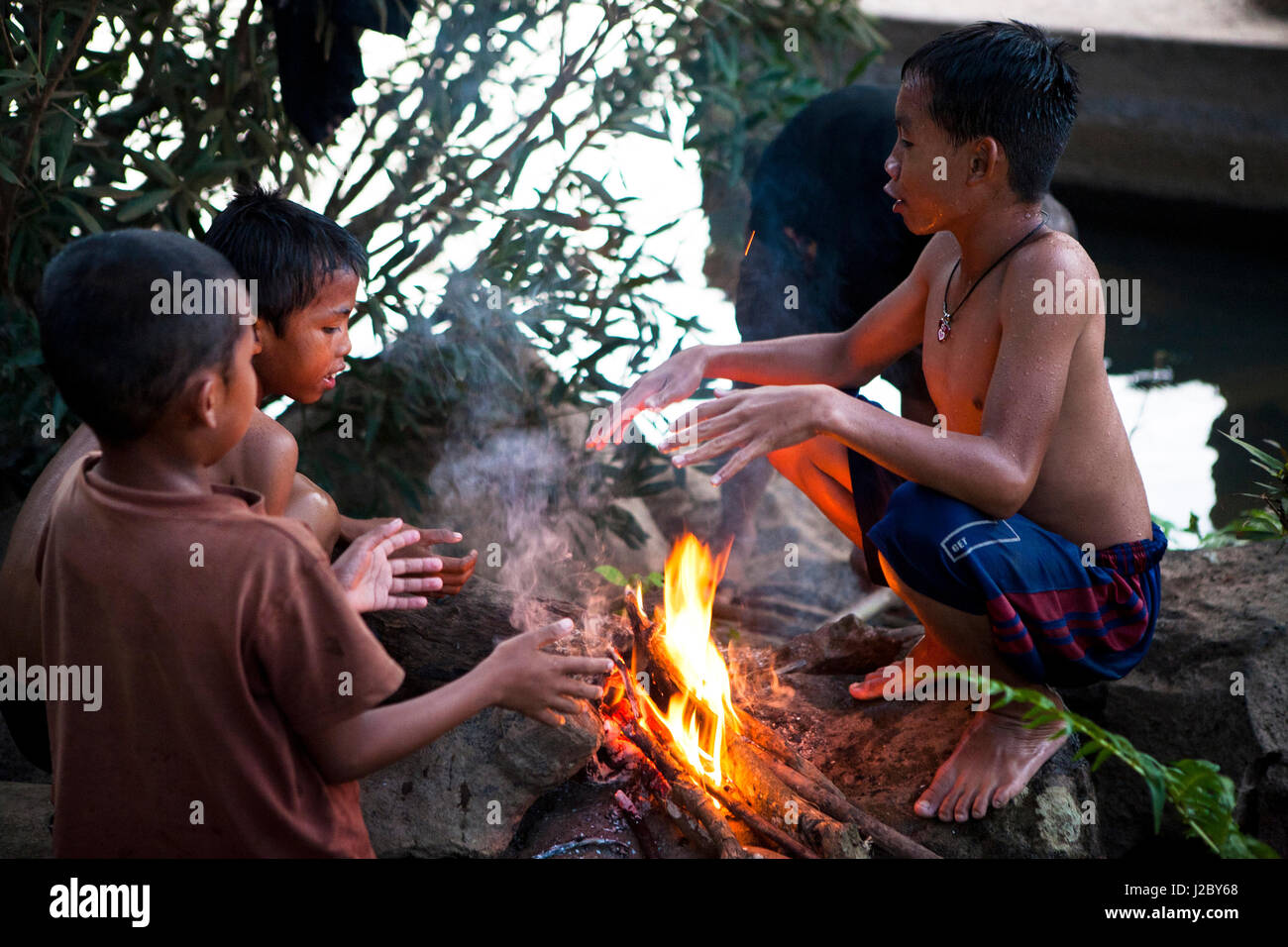 Der verschlafene Fluss Stadt Tad Lo, Laos. Einheimische Kinder wärmten sich durch einen Brand nach dem Angeln im Fluss. Stockfoto
