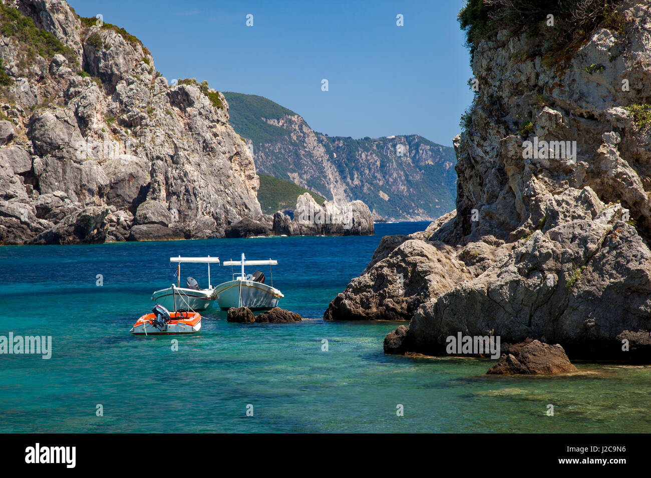 Boote verankert entlang der felsigen griechischen Küste in der Nähe von Paleokastrita auf der Ionischen Insel Korfu, Griechenland Stockfoto