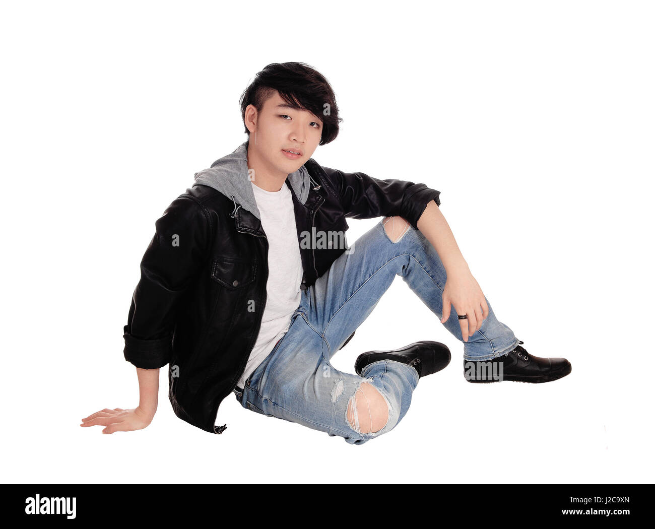 Eine junge asiatische Teenager sitzen in einer schwarzen Lederjacke und zerrissene Jeans auf dem Boden für weißen Hintergrund isoliert. Stockfoto