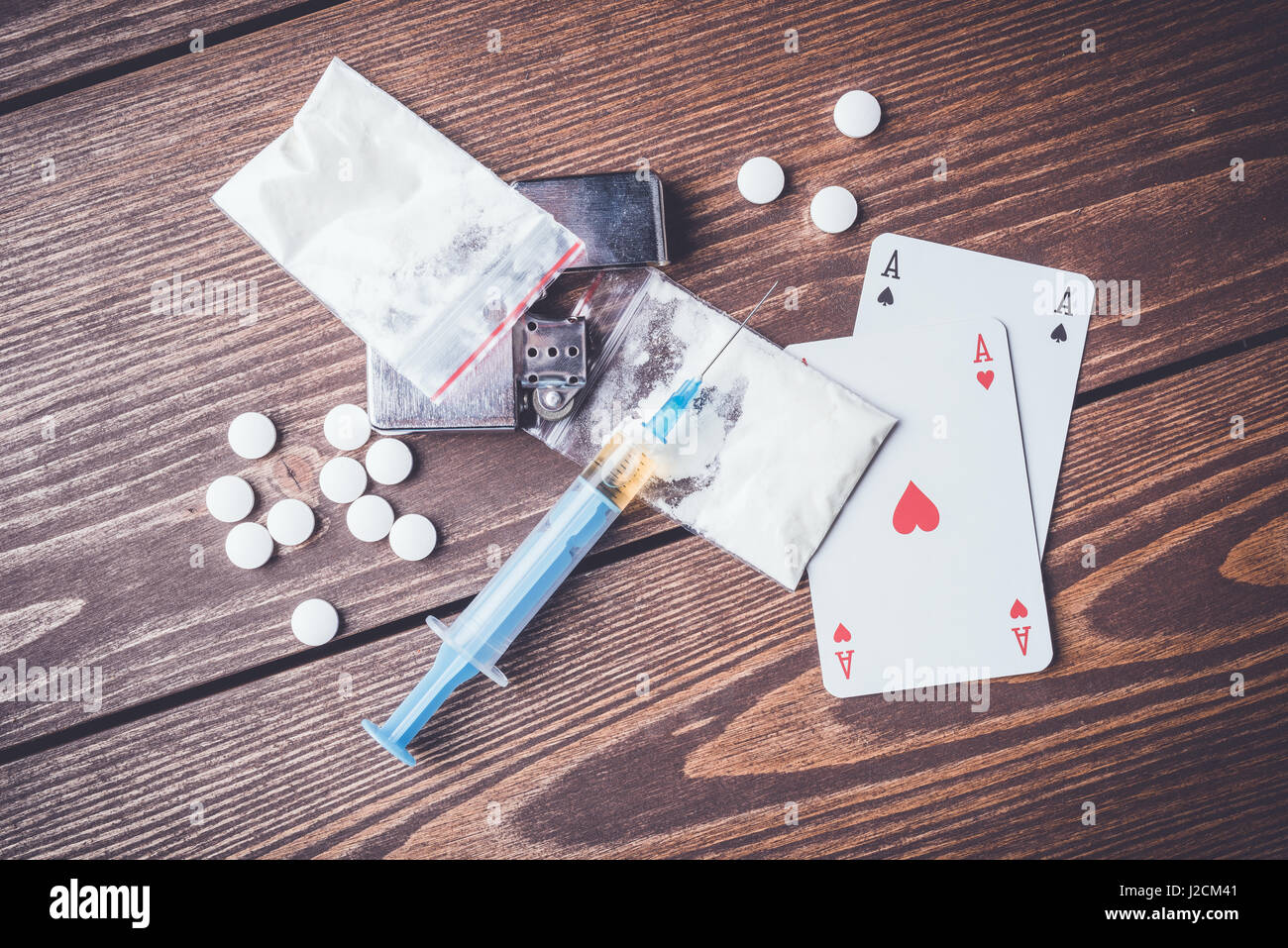 Harte Drogen mit Pillen, Spielkarten und Spritze auf hölzernen Tisch Stockfoto