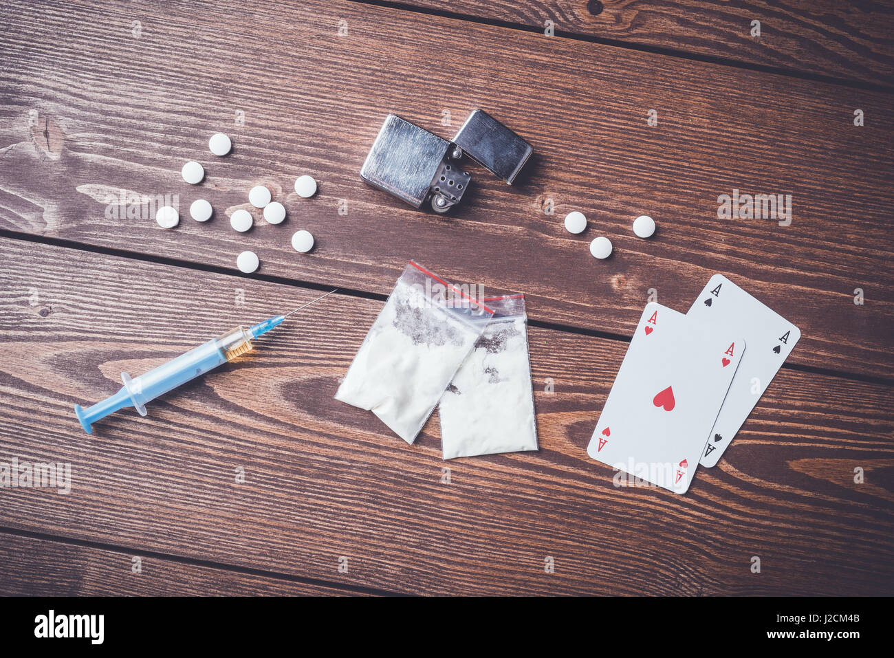 Harte Drogen mit Pillen, Spielkarten und Spritze auf hölzernen Tisch Stockfoto