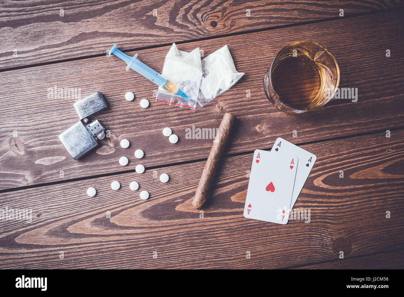 Harte Drogen mit Pillen, Karten spielen, Spritze und Alkohol auf hölzernen Tisch Stockfoto