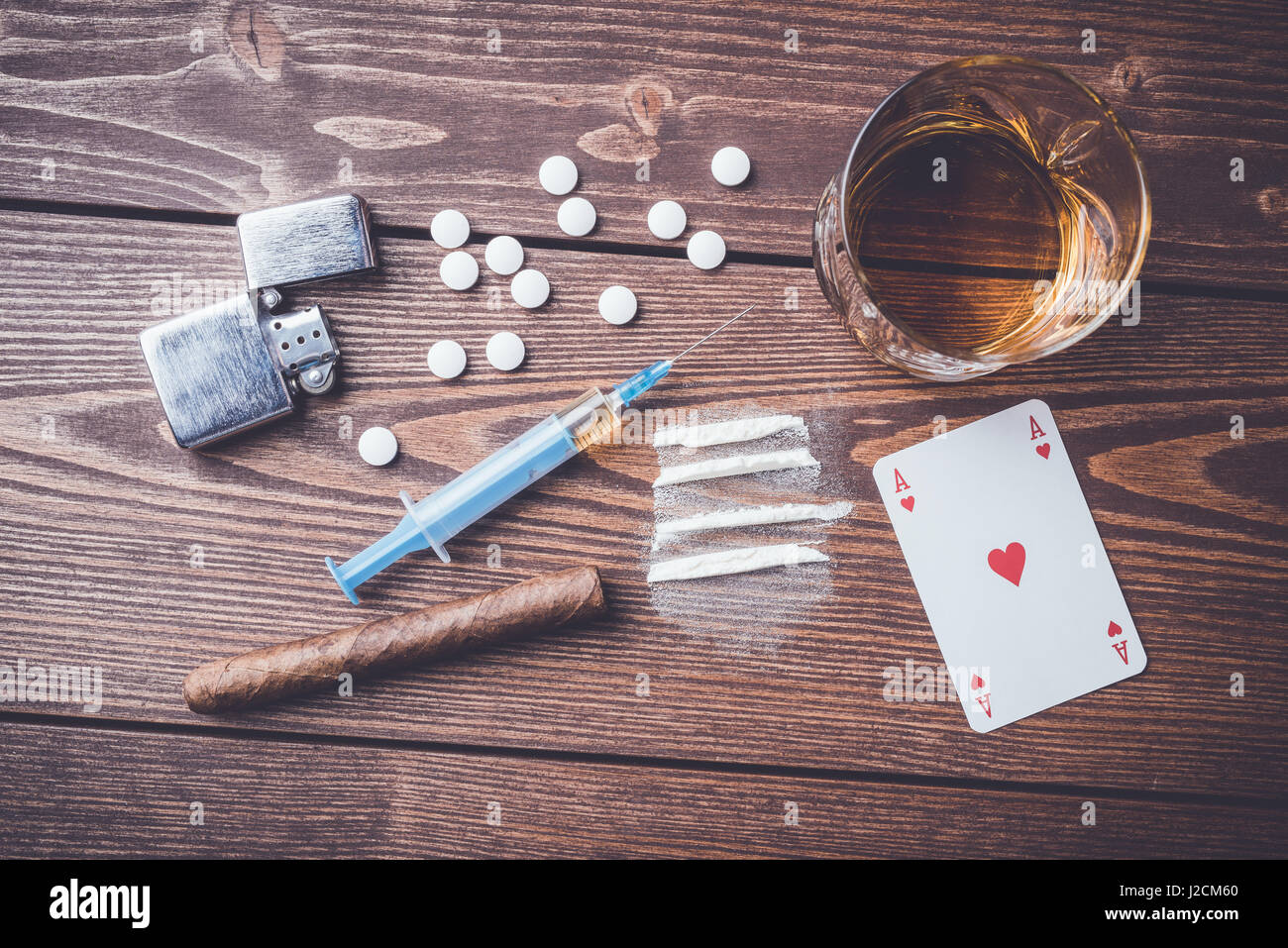 Harte Drogen mit Pillen, Karten spielen, Spritze und Alkohol auf hölzernen Tisch Stockfoto