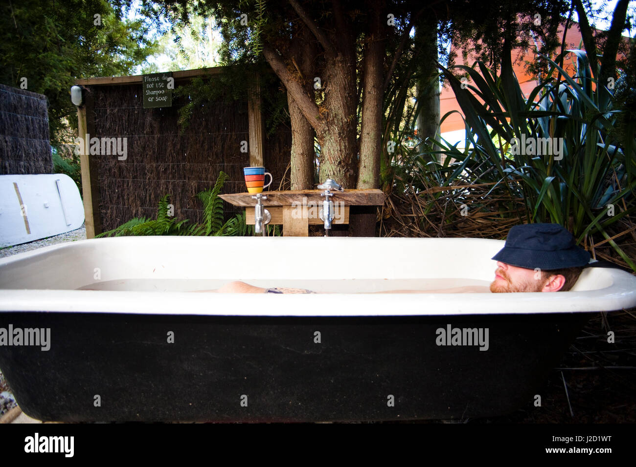 Die Scheune-Herberge entspannen Backpacker in einer einzigartigen alten altmodischen Badewanne im Freien, Abel Tasman National Park, Neuseeland. (PR) Stockfoto