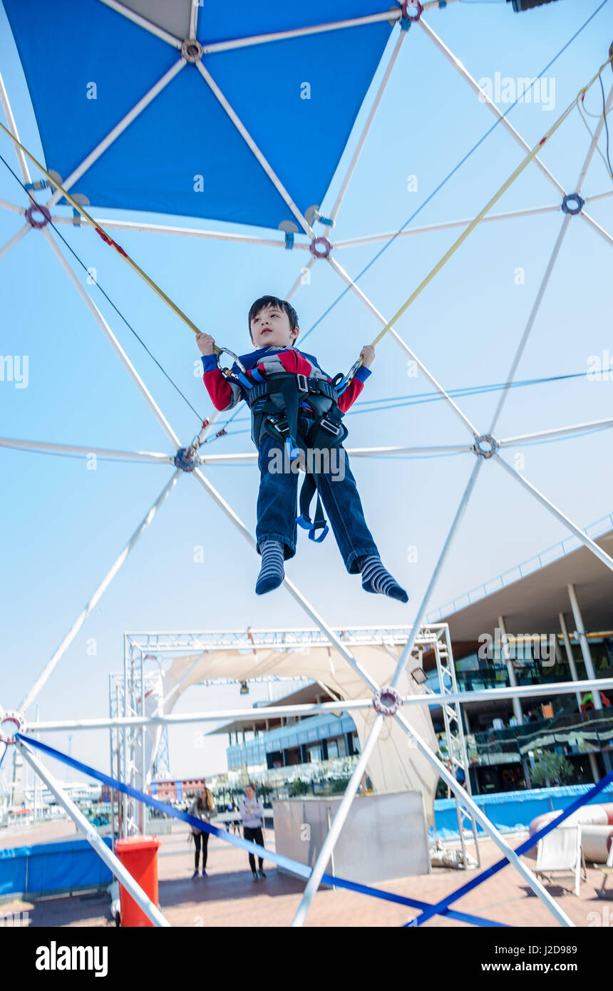 Ein kleiner Junge springt auf einem Trampolin solange Bungie Seile um ihn zu höher hüpfen zugeordnet. Stockfoto