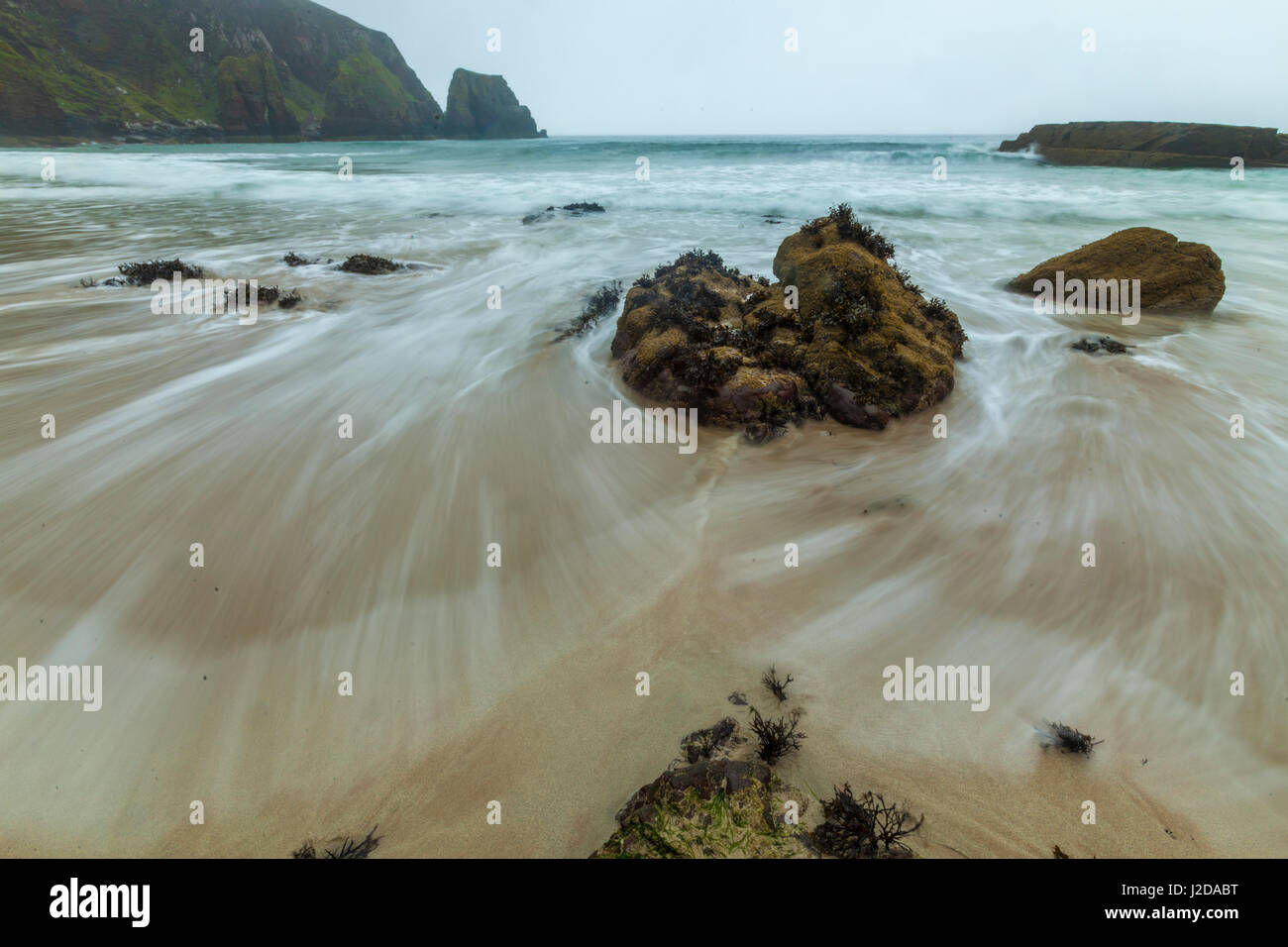 eine Welle von der steigenden Flut spült über den Strand und den Felsen unterhalb der Klippen von Camus Mor, Schottland Stockfoto