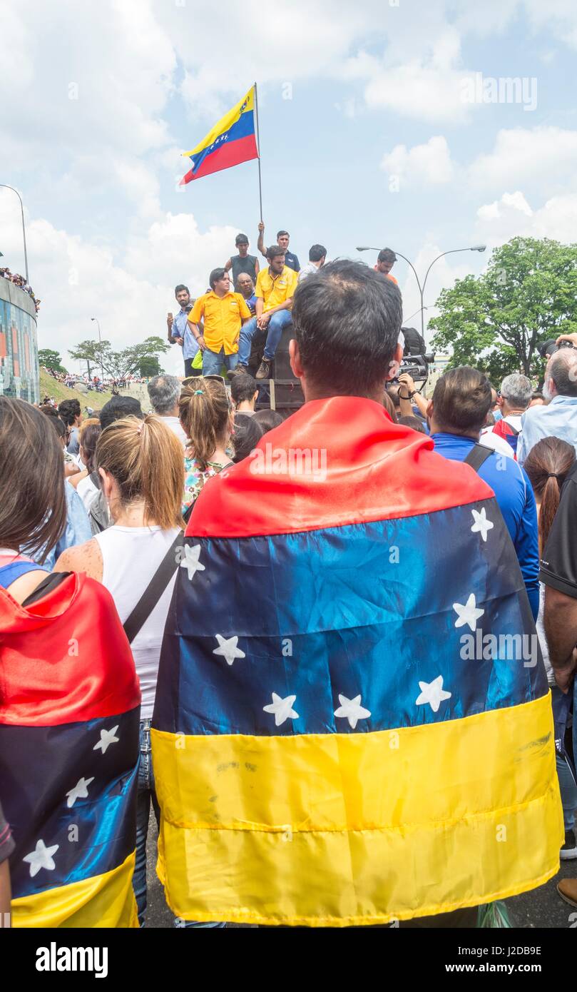 Ein junger Mann mit der venezolanischen Flagge auf seinem Rücken hört auf die Worte der jungen oppositionellen Abgeordneten bei einer Konzentration auf der Autobahn. Am Montag, den 24. April startete die venezolanische Opposition eine neue Protestierende Strategie: eine nationale Sit-In. Ziel ist es, eine "höhere Druck" erreicht durch Blockieren der Hauptstraßen und Autobahnen des Landes und in Platz bleiben für Stunden Stockfoto